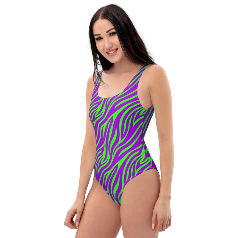 Purple and green neon zebra print one-piece swimsuit with high-cut legs and scoop back, styled in a bold Y2K retro design.