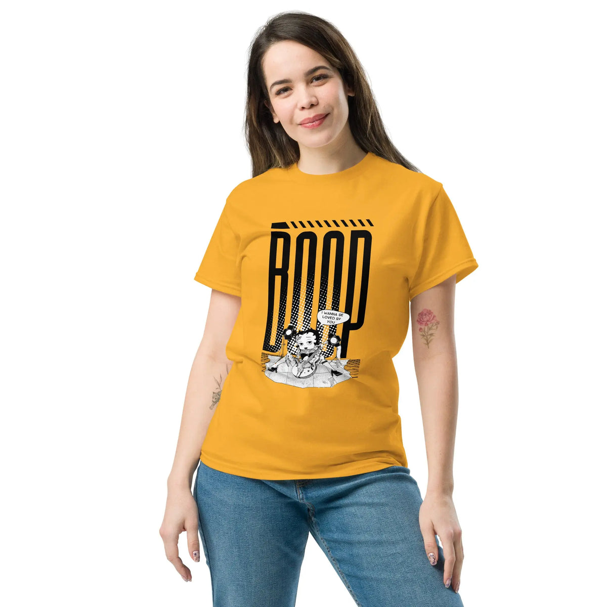 Woman wearing a Gold graphic tee with a Betty Boop-inspired rock star design, styled with blue denim jeans