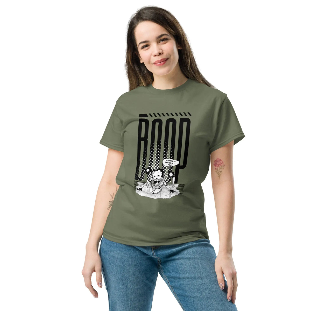 Woman wearing a military green graphic tee with a Betty Boop-inspired rock star design, styled with blue denim jeans