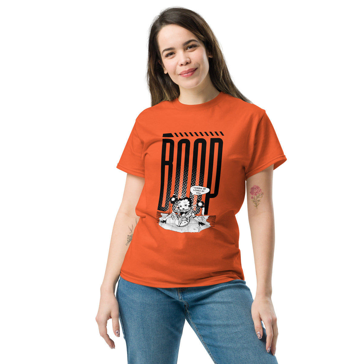 Woman wearing a orange graphic tee with a Betty Boop-inspired rock star design, styled with blue denim jeans