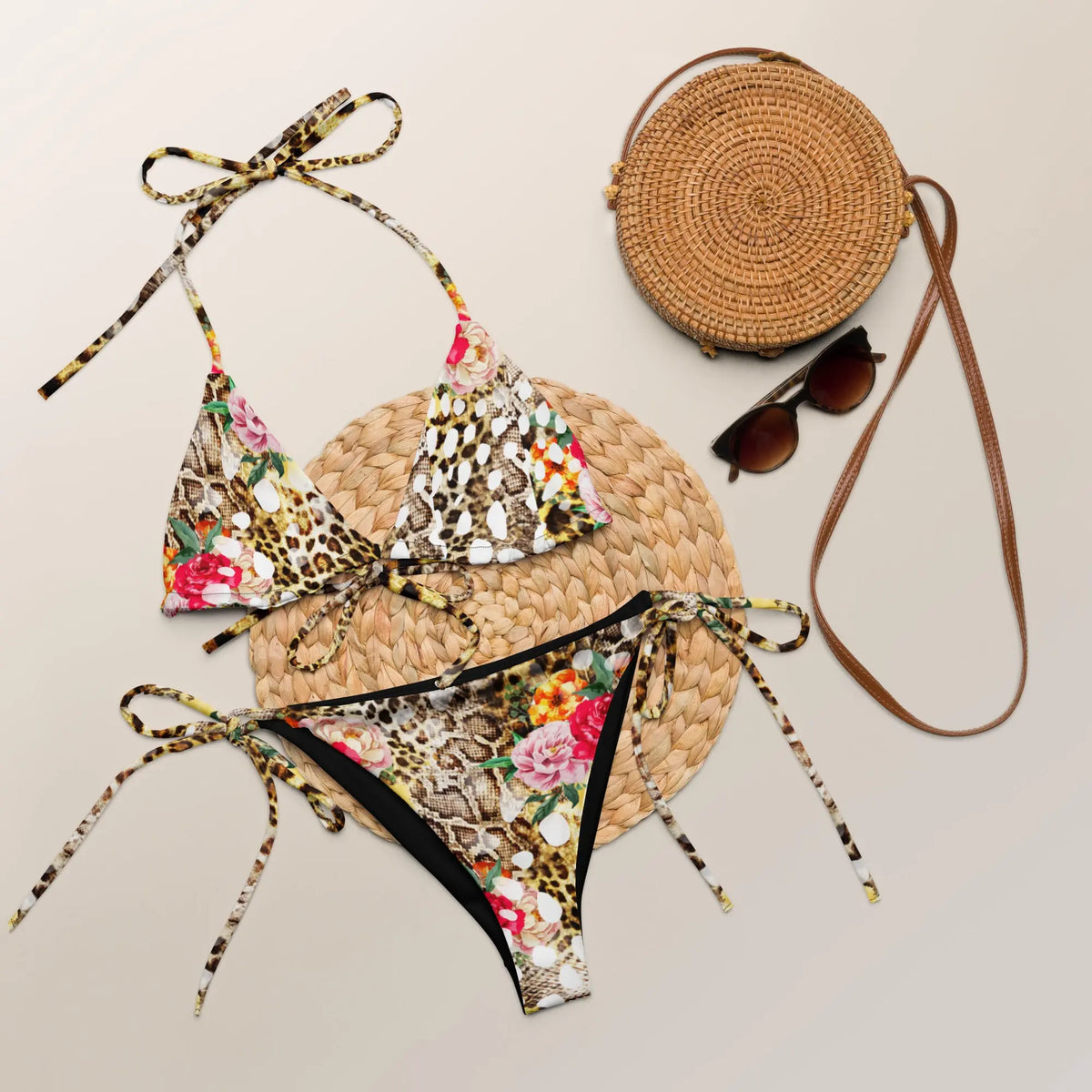 Bikini set with floral and leopard print design, round straw bag, and sunglasses on a light background