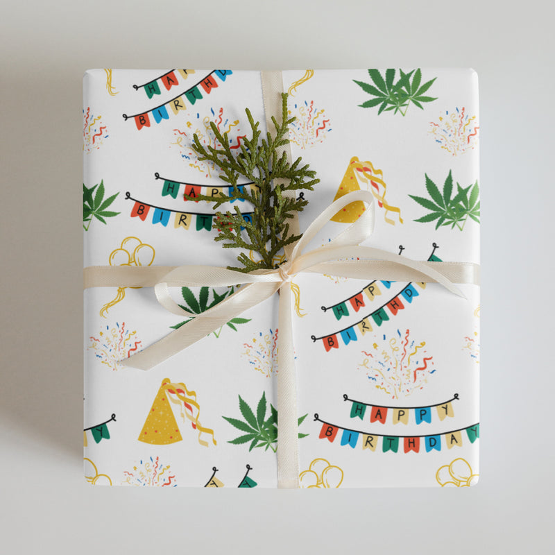 White cannabis-themed birthday wrapping paper with colorful banners, party hats, confetti, balloons, and green leaves