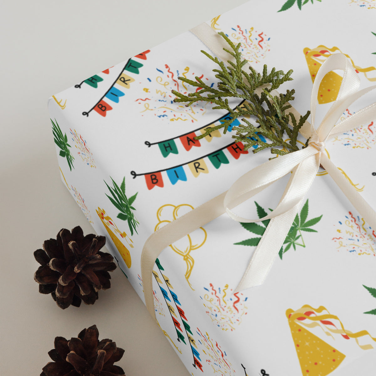 White cannabis-themed birthday wrapping paper with colorful banners, party hats, confetti, balloons, and green leaves