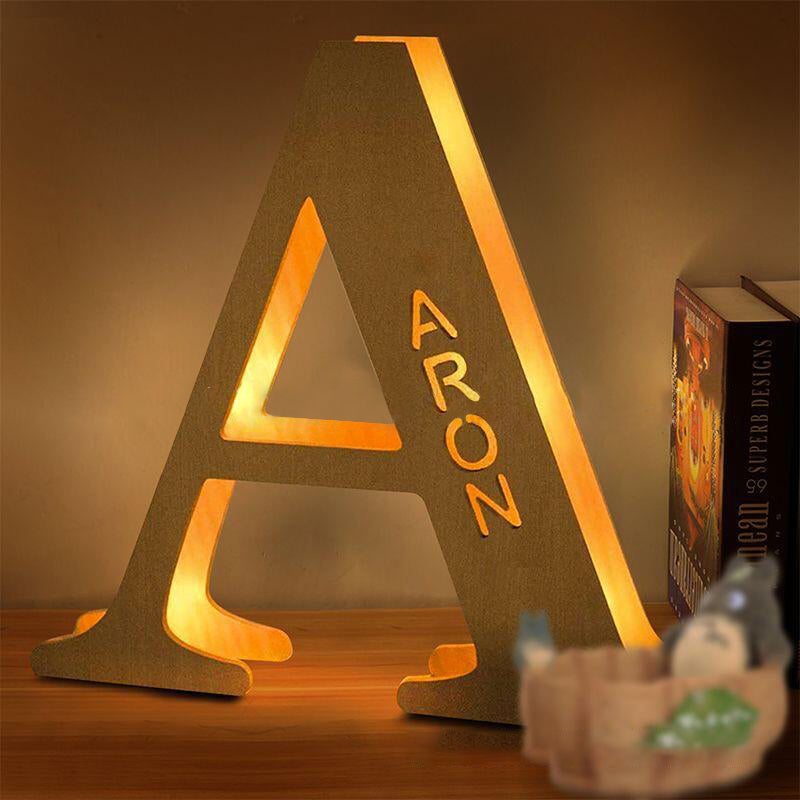 Personalized wooden alphabet LED night light with hollow-engraved letter and custom name illuminated by a soft ambient glow