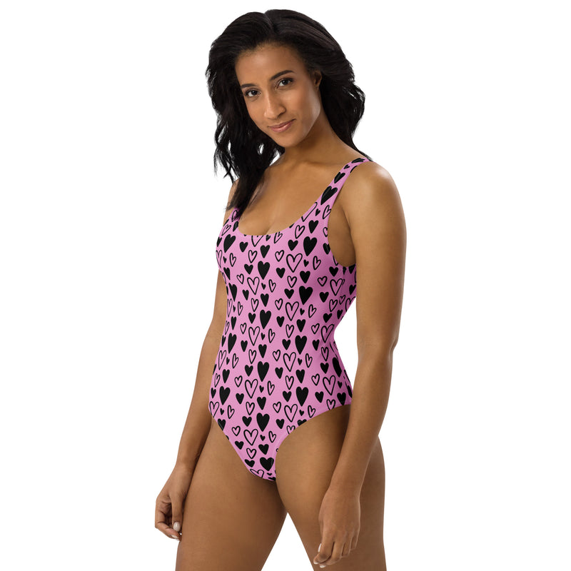 Model wearing a Pink one-piece swimsuit covered in solid and outlined black heart prints with scoop neckline