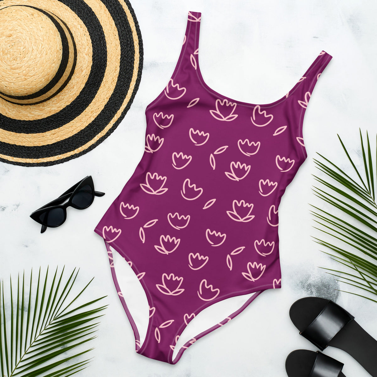 Purple one-piece swimsuit with light pink tulip floral print and scoop neckline swimsuit with white floral pattern, black sunglasses, straw hat, and black sandals on a white background.