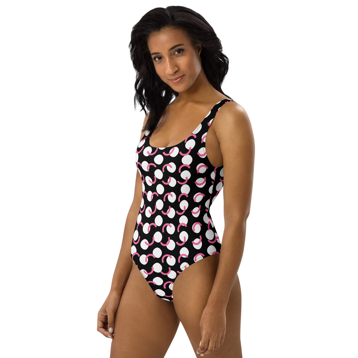 Model wearing  a  Black one-piece swimsuit with white circles and pink curved polka-dot accents, scoop neckline, and cheeky fit