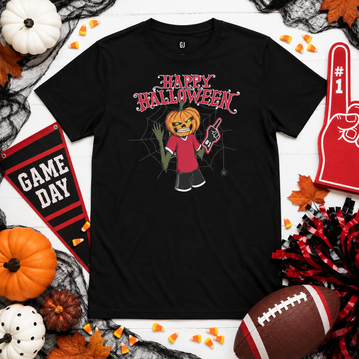 Black Bulldogs Halloween game day T-shirt laid flat with a pumpkin-head fan graphic, surrounded by red-and-black game day decor, foam finger, football, pumpkins, candy corn, fall leaves, and Halloween accents.