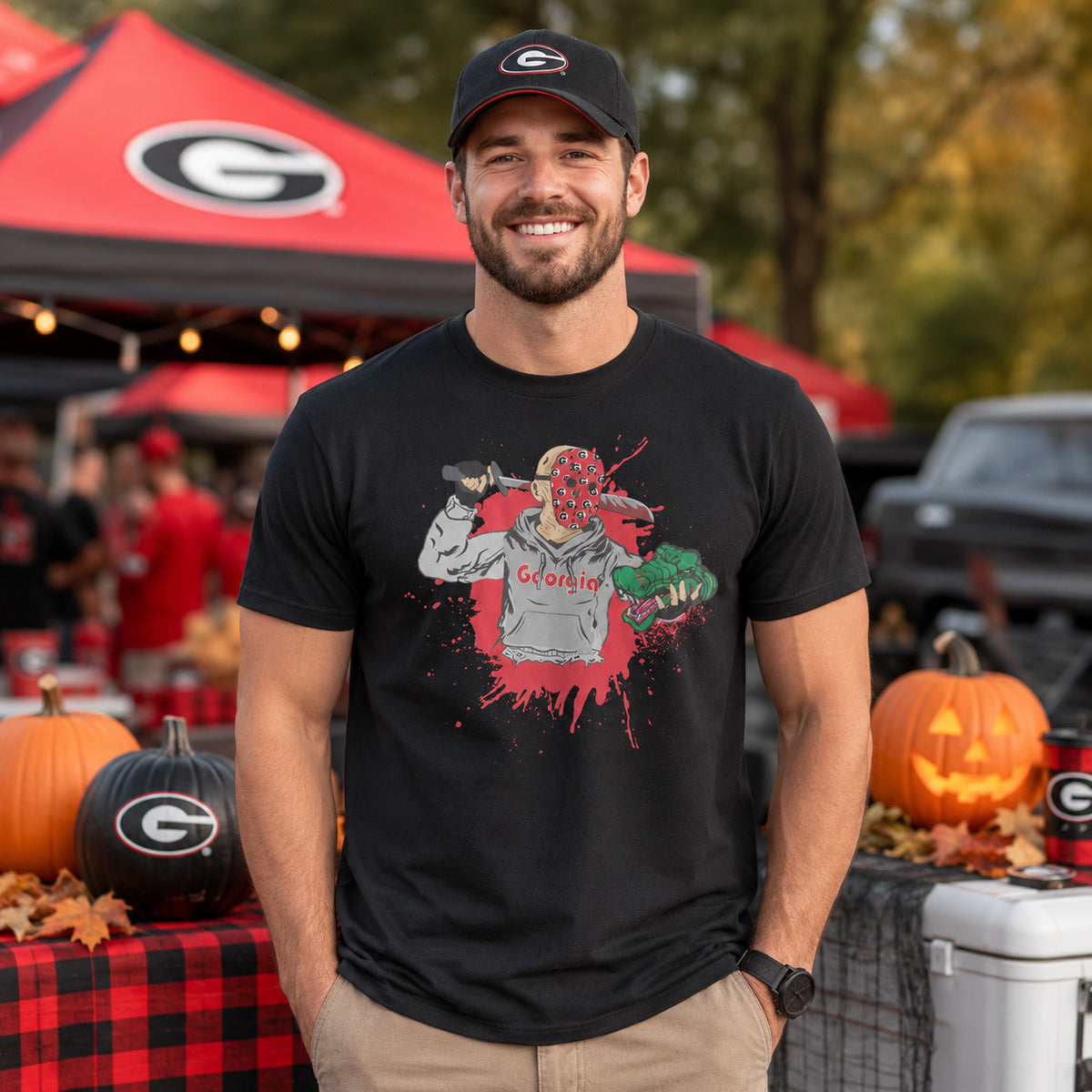 Georgia fan model wearing a black Halloween rivalry game day T-shirt with a slasher-style Georgia graphic at a festive tailgate scene with pumpkins, fall leaves, red-and-black decor, and game day tents.