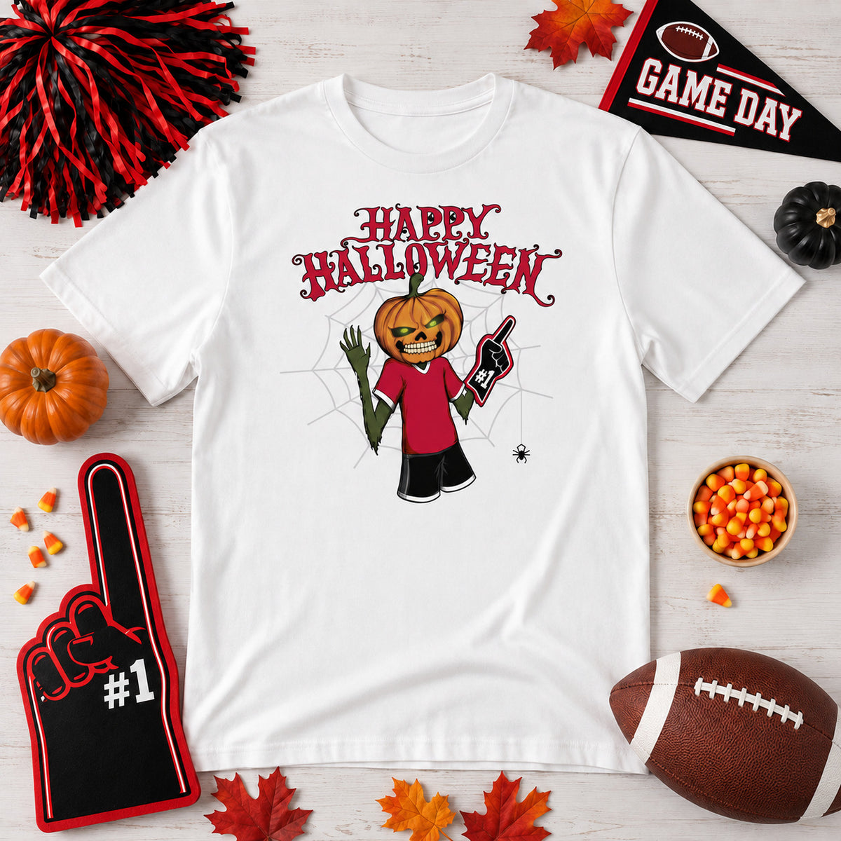 White Bulldogs Halloween game day T-shirt laid flat with a pumpkin-head fan graphic, surrounded by red-and-black game day decor, foam finger, football, pumpkins, candy corn, fall leaves, and Halloween accents.
